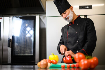 Experienced chef in uniform slicing vegetables in a commercial kitchen with a focus on healthy food prep