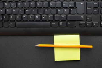 Black keyboard with yellow pen and notepad. Office concept photo.