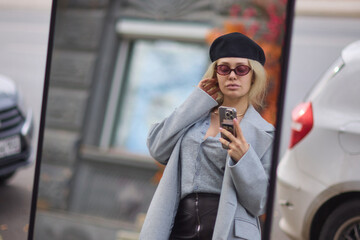 A stylish woman is confidently walking down a busy street, holding a smartphone with flair