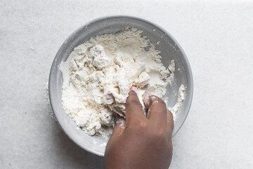 Overhead view of noodle dough being kneaded in a grey bowl, top view of flour and water being mixed to make noodles, process of making hand pulled noodles