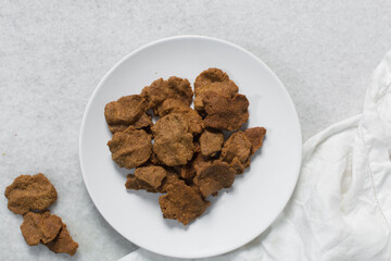 Overhead view of kuli-kuli on a white plate, top view of nigerian groundnut cakes on a plate, fresh homemade nigerian kulikuli on a ceramic plate