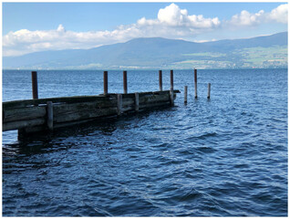 A photograph of a lake in Switzerland, a wooden dock juts into the water