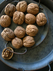 An overhead photograph of walnuts in their shells on an antique plate, warm and inviting