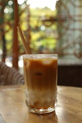 Glass of refreshing iced coffee and straw on wooden table outdoors