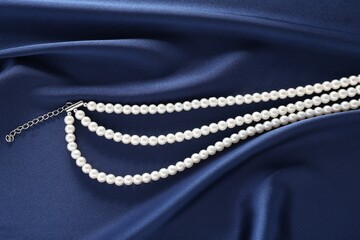 Elegant pearl necklace on dark blue fabric, top view