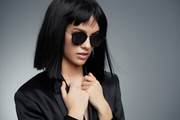 Beautiful young woman with black hair, wearing sunglasses and a black suit, standing confidently...
