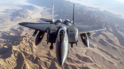 A grey F-15E Strike Eagle fighter jet flies over a mountainous desert landscape.