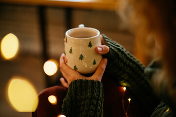 Christmas mug held in woman hands, capturing the cozy holiday spirit. Close-up of woman hands...