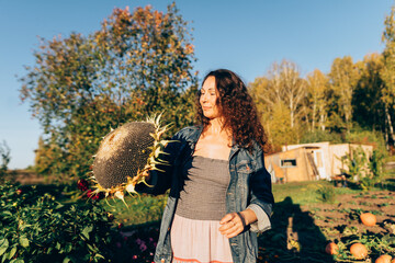 Middle-aged woman with sunflower, embracing the joy of the harvest season and fertility. Woman celebrating the harvest festival, holding a sunflower on her rural farm with a smile