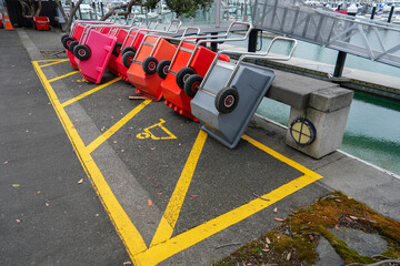 Colorful carts tipped over on a marina sidewalk, showcasing urban life, waterfront activity, and interesting composition at a busy harbor location with parking lines.