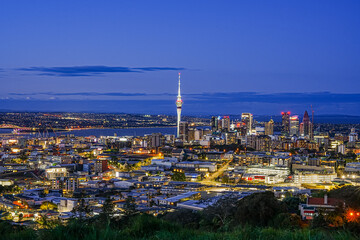 Stunning Aerial View of Auckland City Skyline at Dusk with Illuminated Buildings and Sky Tower Rising Against a Beautiful Blue Sky and Ocean