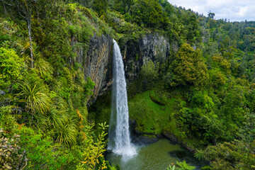 Majestic waterfall cascading down rocky cliff surrounded by lush greenery and vibrant foliage in a serene natural landscape under a cloudy sky