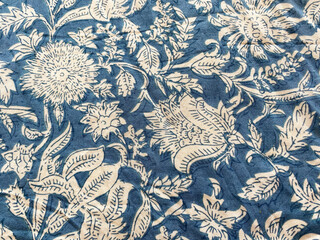 blue indigo cotton fabric showcases an intricate white floral outline, creating a delicate contrast that exudes elegance and charm. © blendindia