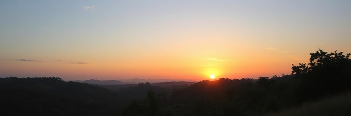 Fototapeta premium A serene evening sky with the setting sun casting a warm orange glow over rolling hills and lush greenery, sunset landscape, countryside, hilltop view