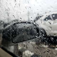 Rain drops on car window with blurred background of parked cars. A moody, rainy day captured through droplets on glass. Perfect for conveying calm, reflection, and rainy weather vibes.