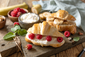 Breakfast concept, dessert french pastry. Tasty freshly baked open croissants with cream cheese and raspberry on a rustic background.
