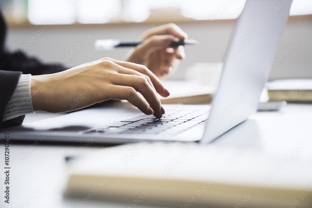 Poster Female hands in sharp focus typing on a modern laptop keyboard, office environment in soft blur behind