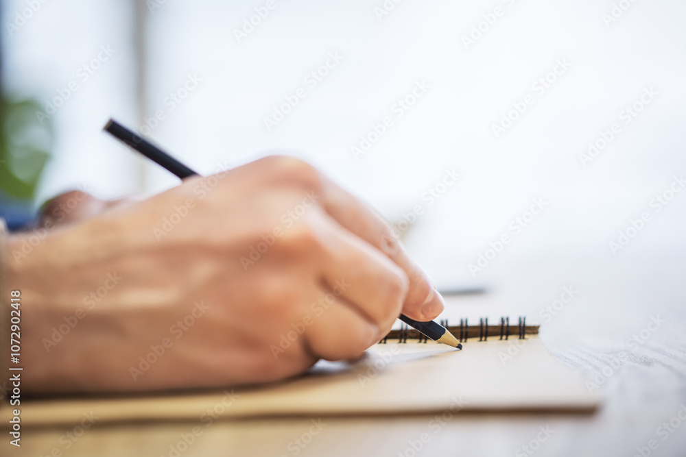 Poster Close perspective of a man's hand making entries in a notepad, with a soft blur in the surrounding
