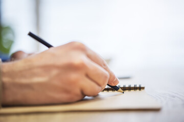 Close perspective of a man's hand making entries in a notepad, with a soft blur in the surrounding