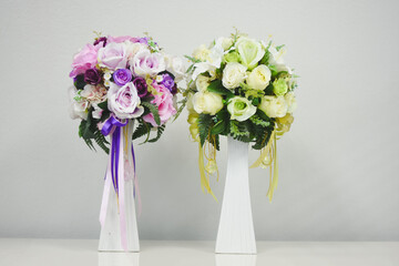 two floral arrangements in white vases. The arrangement on the left consists of various shades of...