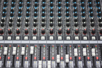 close-up view of an audio mixing console. The console features multiple rows of knobs and sliders.