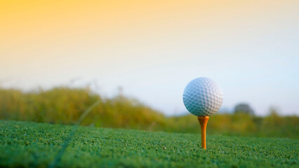 Golf ball on tee in beautiful golf course with sunset.