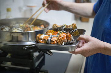 Hands of a woman using chopsticks to pick up cooked hairy crabs in a steamer. Delicious Yangcheng...
