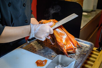 Hands of a chef holding a kitchen knife, carving roast Peking duck in a restaurant.