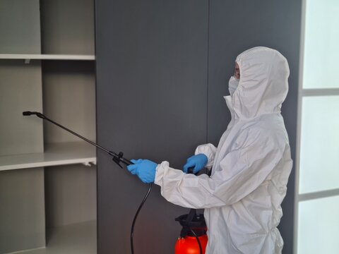 Pest control technician sanitizing a shelf in a modern home using a spray device