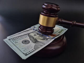 Legal gavel resting on a stack of hundred dollar bills in a courtroom setting, symbolizing justice...