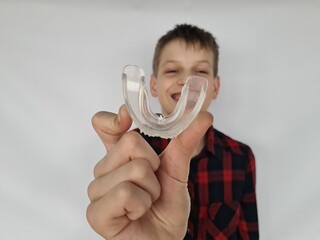 A boy smiles while holding a clear mouthguard in front of a plain background