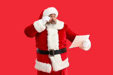 Shocked Santa Claus reading letter on red background