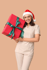 Beautiful female massage therapist in Santa hat with gift box on brown background