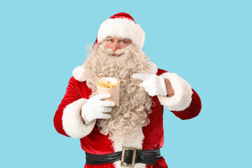 Santa Claus pointing at tasty french fries on blue background