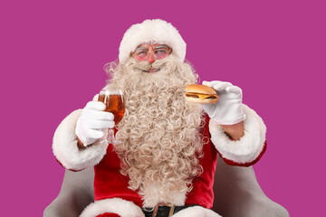 Santa Claus with glass of beer and tasty burger in armchair on purple background