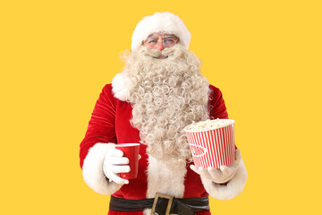 Santa Claus with cup of cola and tasty popcorn on yellow background
