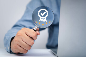 A person holding a magnifying glass over a laptop, emphasizing quality and assurance with a...