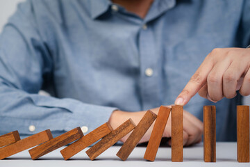 A person stabilizing wooden dominoes with their finger, symbolizing the balance and chain reaction...
