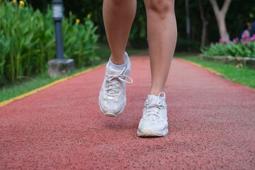 Close-up of a person jogging on a red track, showcasing athletic shoes and active lifestyle in a vibrant park setting.