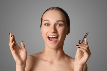 Young woman correcting shape of her eyebrows on grey background