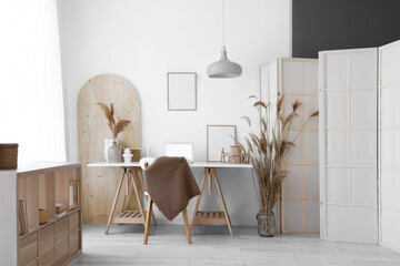 Modern workplace with laptop, shelving unit and folding screen