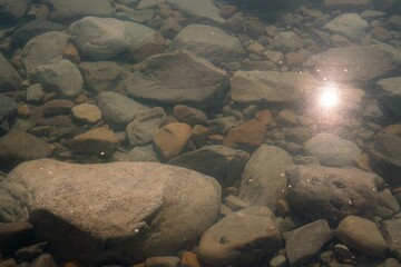 Sun Reflection and Floating Particles on Clear Water Surface of Rocky Lake