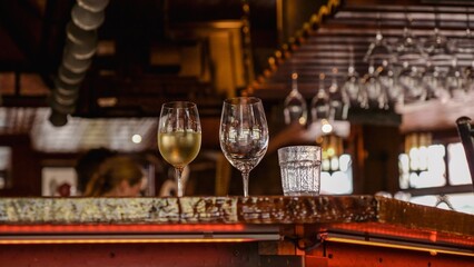 Two elegant wine glasses with golden liquid on a shiny bar counter with blurred background