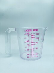 A transparent plastic measuring cup with pink graduations, showing precise measurements from 10 to...