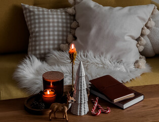 Cozy homely atmosphere - Christmas decor, candles, books on a wooden table near the sofa