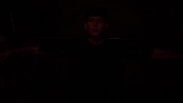 A young man is handcuffed to a wall in a dark room with a flashing red light, silhouette. A dark prison room with old rusty walls and antique shackles. The room of horrors.