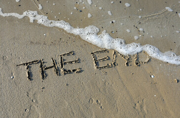 words the end written on a beach with a wave about to erase them