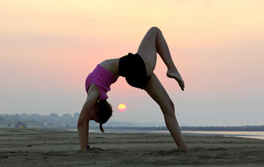 woman performing backbend exercise with sun in the distance