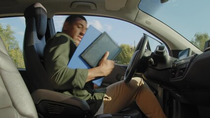 Confident handsome African American businessman driver in casual clothes entering car, buckling up seat belt and pushing engine start button while driving electric vehicle in city during road trip.