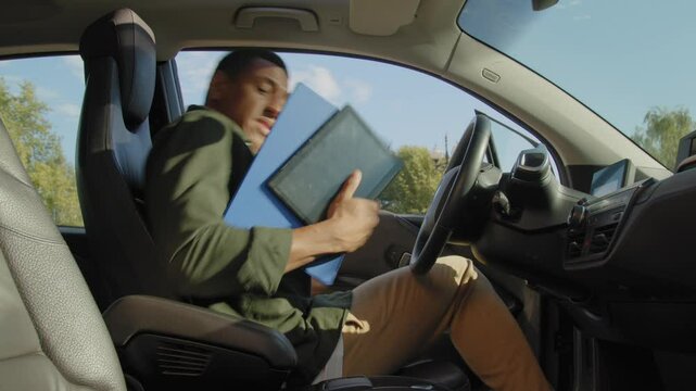 Confident handsome African American businessman driver in casual clothes entering car, buckling up seat belt and pushing engine start button while driving electric vehicle in city during road trip.